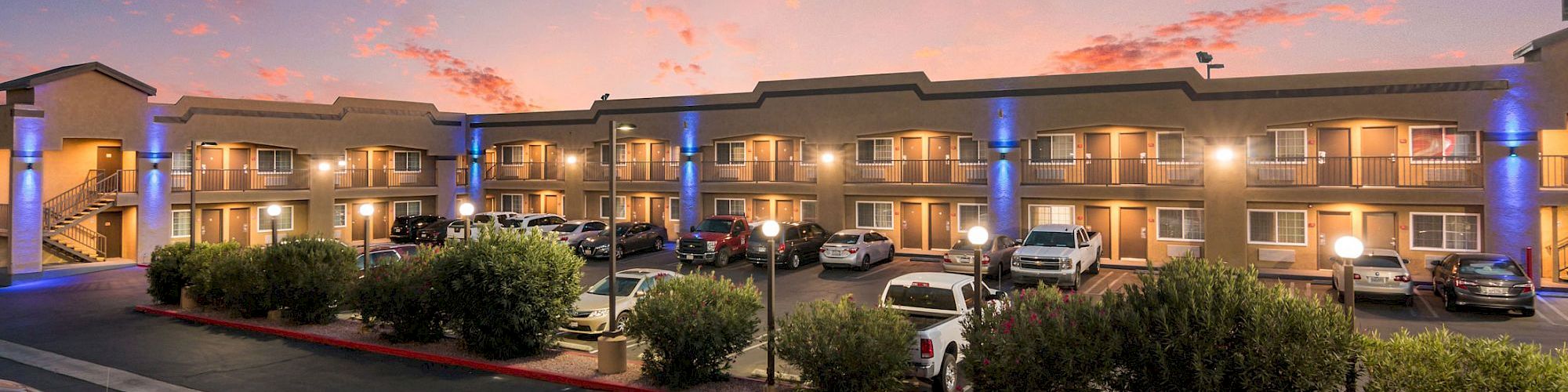 A two-story motel with parked cars and illuminated balconies under a vibrant sunset sky.