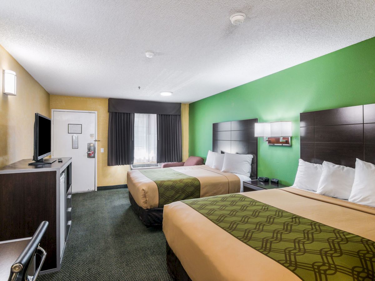 A hotel room with two double beds, a TV, a desk and chair, and vibrant green and beige decor behind the beds ending the sentence.