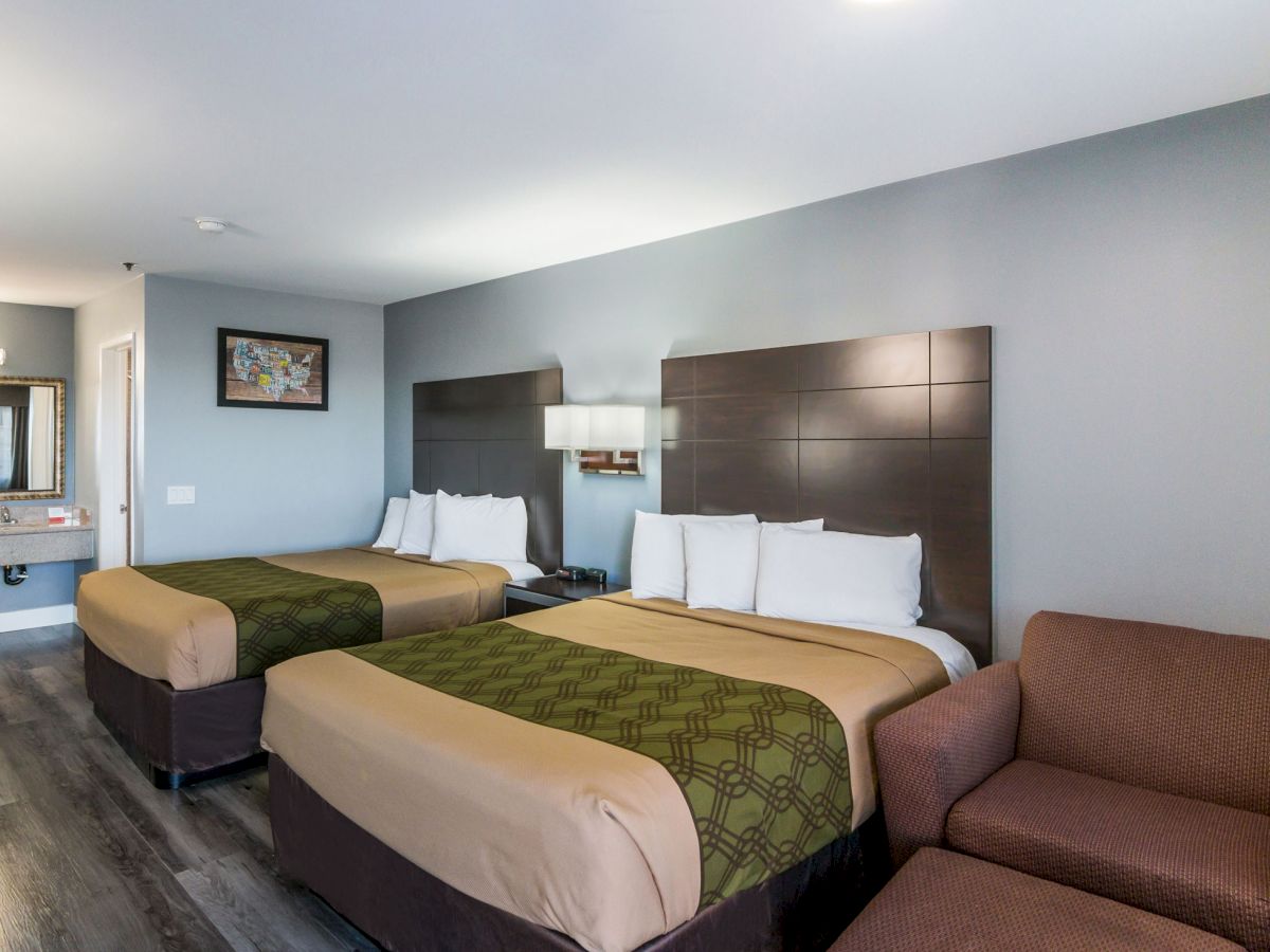 A hotel room with two double beds, a chair, bedside lighting, a vanity area with a sink and mirror, and modern decor in neutral tones.