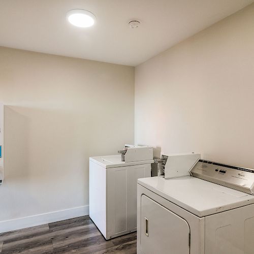 The image shows a laundry room with a vending machine for soap, bleach, and softeners on the wall, a washing machine, and a dryer.