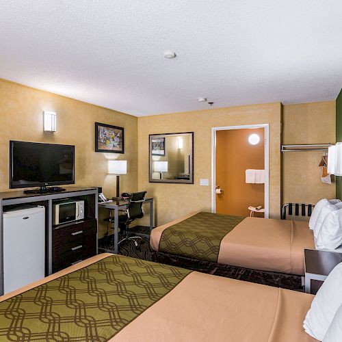 The image shows a hotel room with two beds, a TV, a mini-fridge, a desk, and a green accent wall. There is a window and a doorway visible.