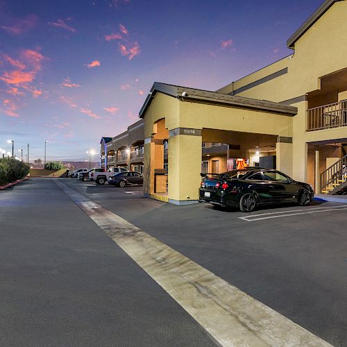 The image depicts the exterior of a motel or apartment complex at sunset, with parked cars and illuminated buildings.