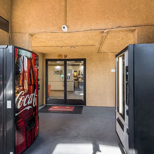 The image shows the entrance to a building with vending machines on either side, one being a Coca-Cola machine, under an overhang.