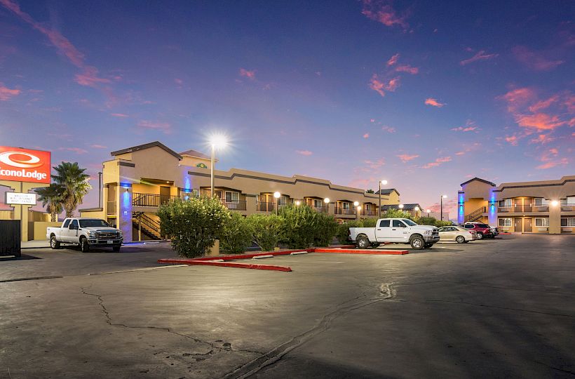 The image shows an Econo Lodge motel at dusk with parked cars, two-story buildings, and a lit sign and surroundings.