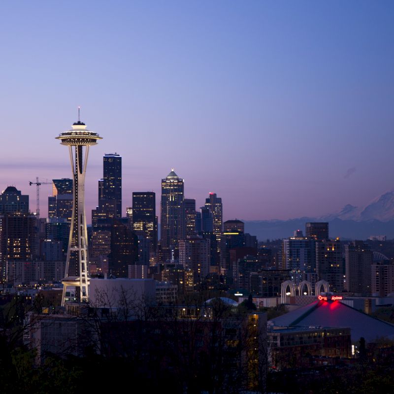 This image captures a twilight view of the Seattle skyline, featuring the Space Needle prominently and Mount Rainier in the background.