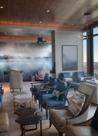 This image shows a modern lounge area with multiple comfortable chairs, tables, and a scenic window view of a body of water and a Ferris wheel.