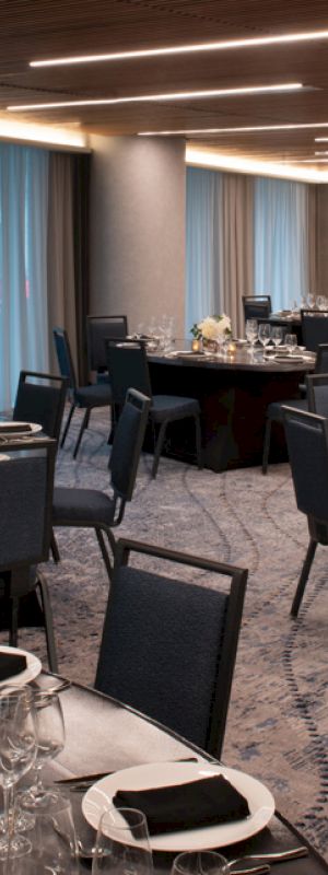 The image shows an elegantly arranged banquet hall with round tables set for dining, featuring dark tablecloths, folded napkins, and floral centerpieces.