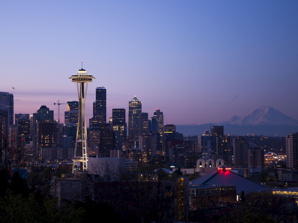 The image shows the Seattle skyline at twilight, featuring the Space Needle prominently, with Mount Rainier visible in the background.