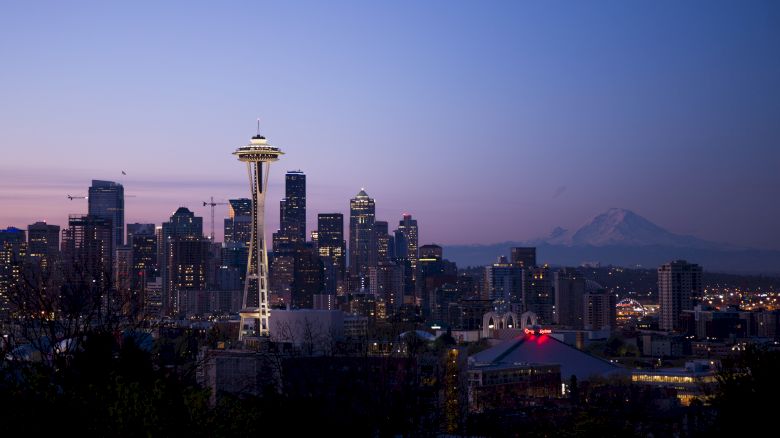 The image shows the Seattle skyline at twilight, featuring the Space Needle prominently, with Mount Rainier visible in the background.